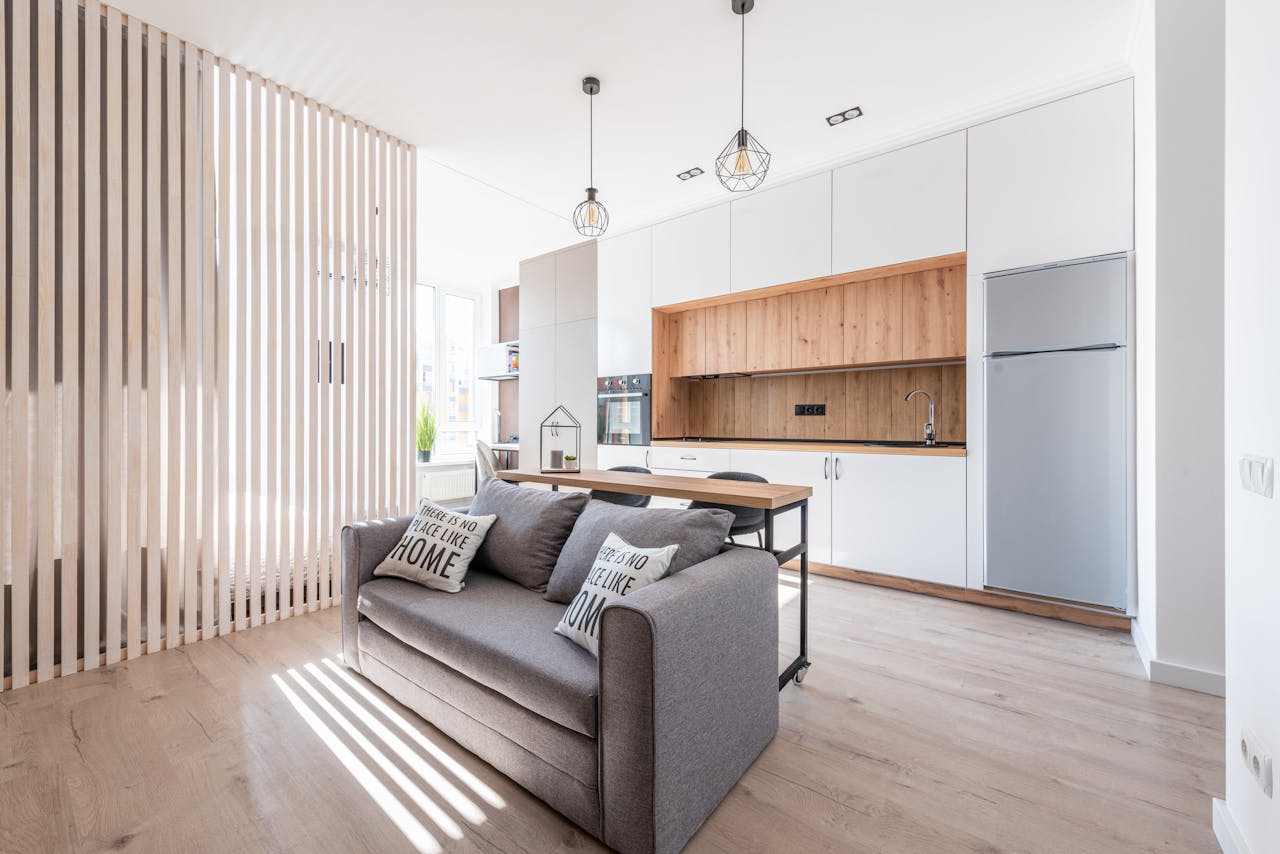 hero-img-01 Interior of contemporary open plan kitchen with white cabinets and cozy sofa with cushions in sunlight