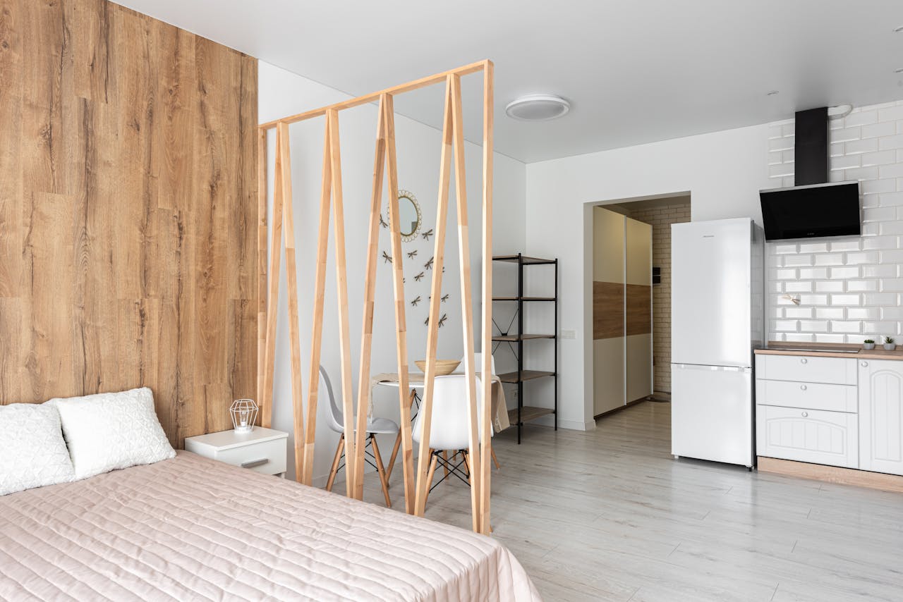 about-01 Bed with cushions and cover against wooden partition and fridge on parquet with chairs at home in daylight